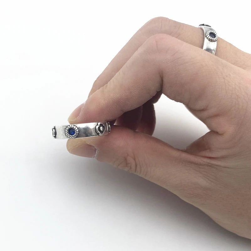 Hand holding a silver ring with a blue stone on a white background