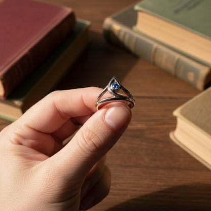 Hand holding a silver ring with a blue gemstone in front of old books on a wooden surface