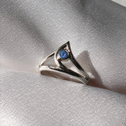 Silver ring with a blue gemstone on a silver fabric background