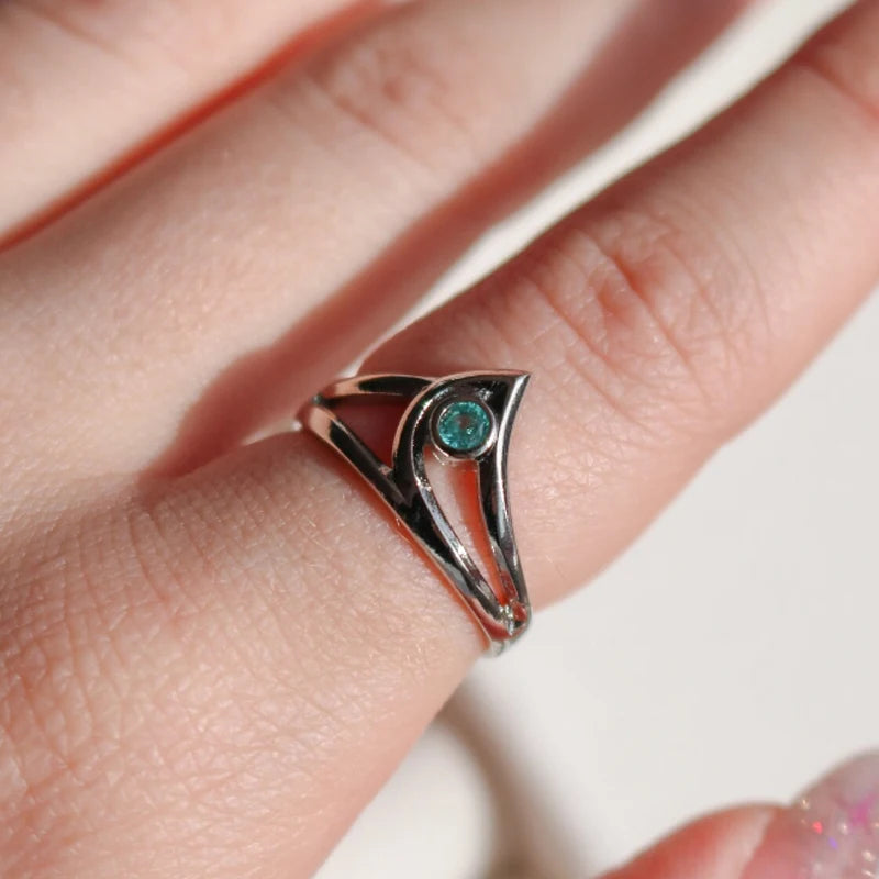 Silver ring with a green gemstone on a finger against a neutral background