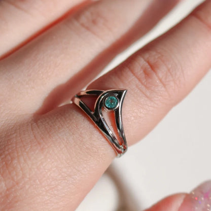 Silver ring with a green gemstone on a finger against a neutral background