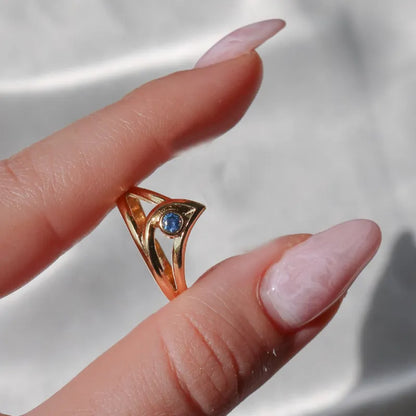 Gold ring with a blue gemstone on a finger against a neutral background