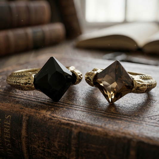 Two versions of Marvolo Gaunt’s Horcrux ring with black and smoky quartz Resurrection Stones resting on an antique book.